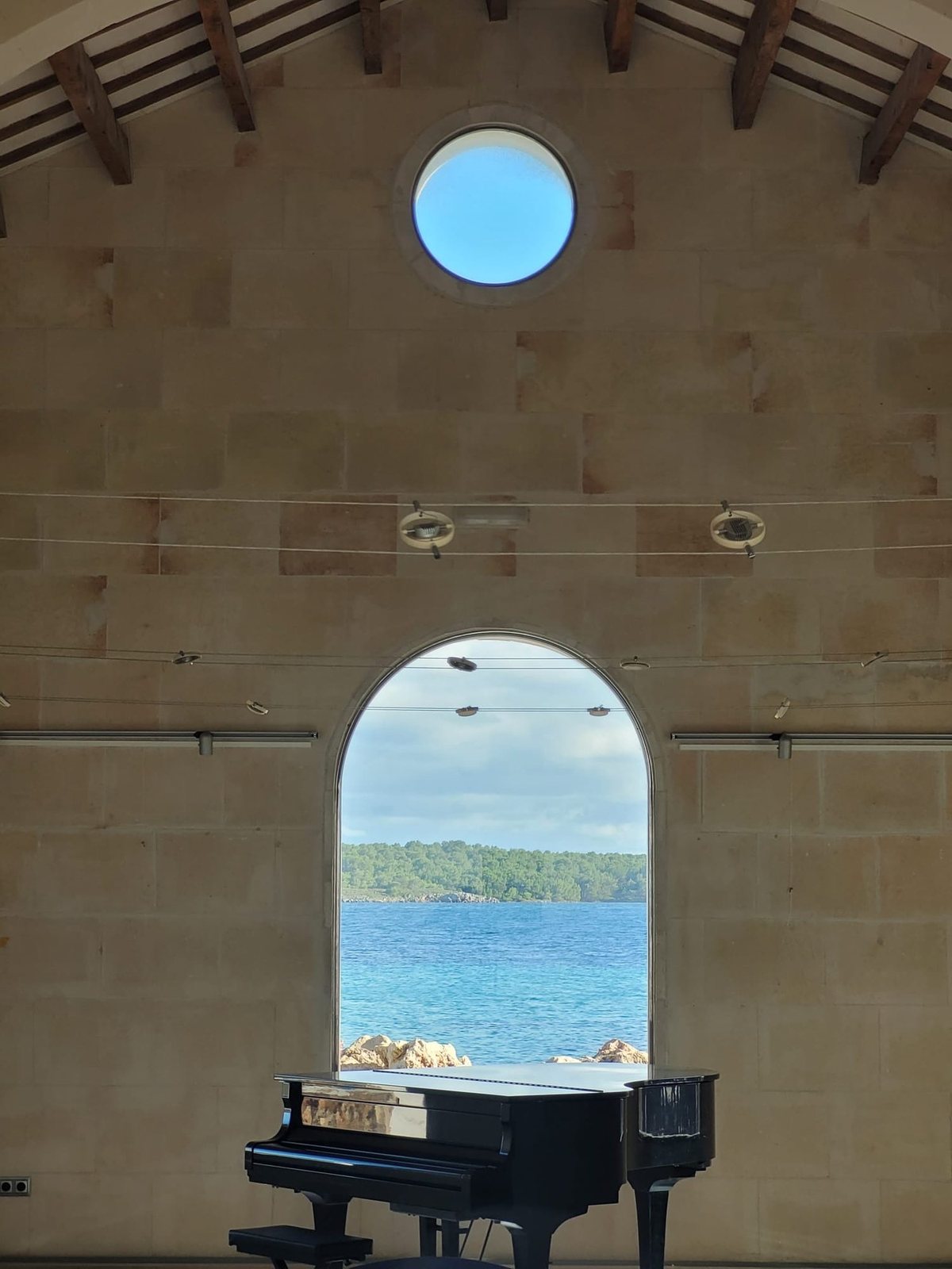 Grand piano in front of an arched window facing the sea